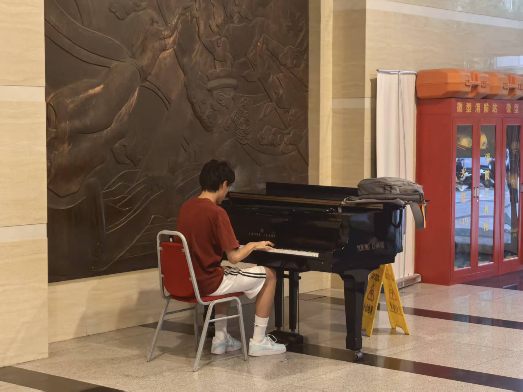 Daniel playing a grand piano in a lobby with a bronze relief wall